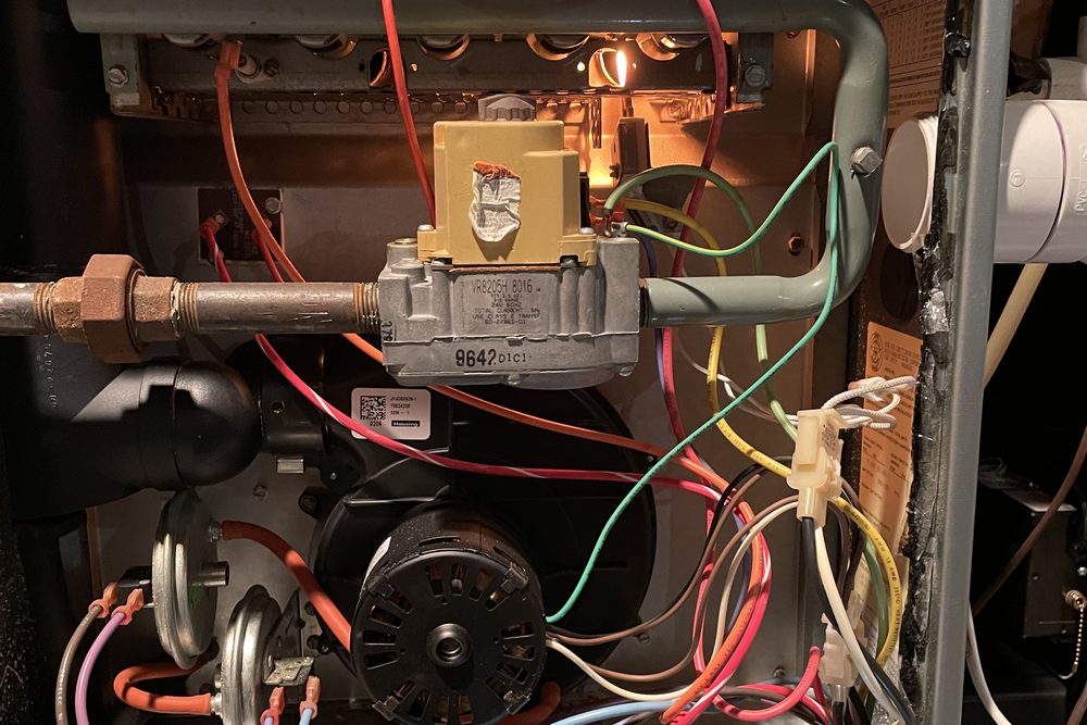 Open gas furnace showing gas valve, inducer motor and lit burners